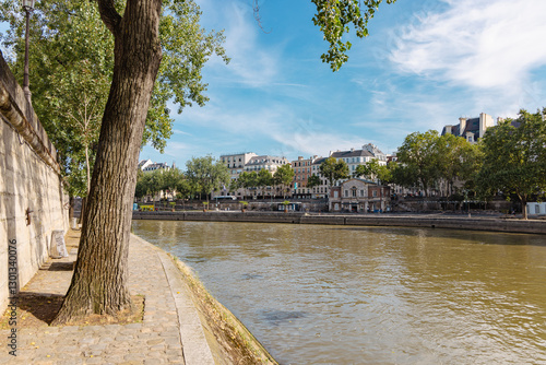 Obraz na płótnie Easy stroll next to the seine river in paris with view of lazy river, trees and houses aligned next to the river. w salonie