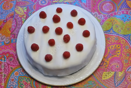 Wallpaper Mural Eine Fondant Torte mit Himbeeren drauf auf einer Tortenplatte mit goldenem Rand. Die Platte steht auf einer sehr bunten Tischdecke mit lila, grün, rosa, blau, orange und weißen Motiven.

 Torontodigital.ca