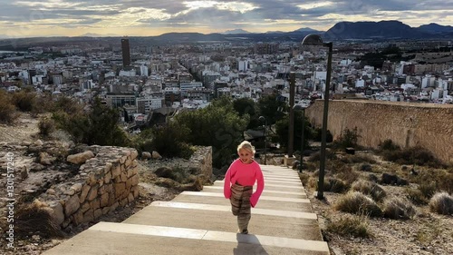Young girl running up outdoor stairs with a cityscape in the background, captured in slow motion