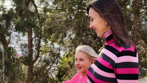 Slow motion video of a mother and daughter enjoying a walk in a park, holding hands and smiling. Medium shot