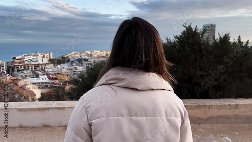 Scenic coastal cityscape, female tourist walking to observation deck. Viewpoint and contemplating picturesque urban landscape at sunset with serene mediterranean atmosphere