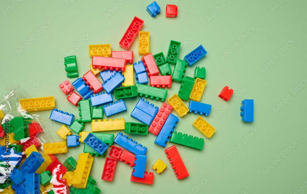 Scattered plastic multi-colored parts of children's construction set on green background, top view Scattered plastic multi-colored parts of children's construction set on green background, top view
