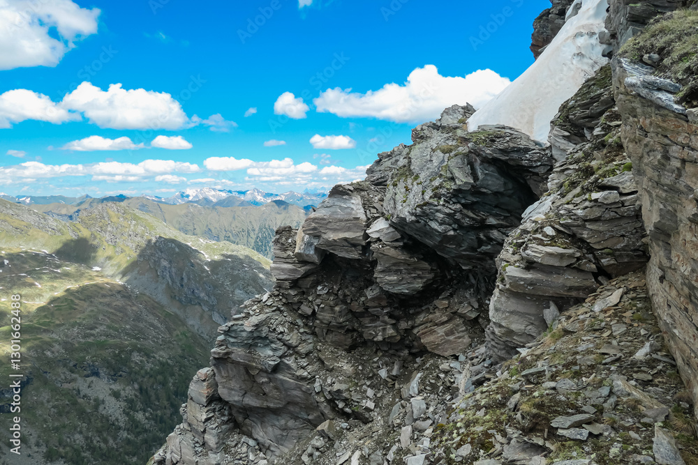 Rugged cliff face drops sharply from Reitereck peak in Carinthia, Austria. Panoramic view of distant mountains. Dramatic beauty of Ankogel Group in Lieser-Malta valley. Remote wilderness Austrian Alps