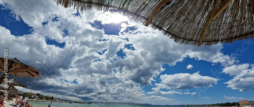Sunny beach day with dramatic clouds and straw parasols
