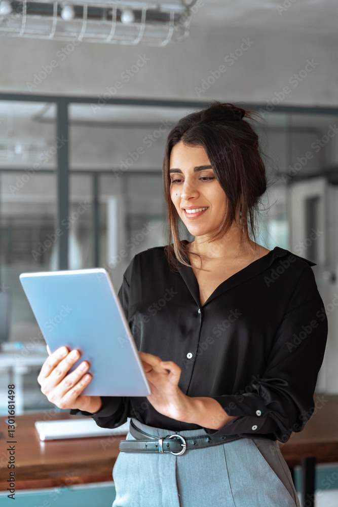 30s Latin Hispanic young professional business woman working on touchscreen computer. Middle eastern Indian businesswoman CEO holding digital tablet using tab application standing in office. Vertical 30s Latin Hispanic young professional business woman working on touchscreen computer. Middle eastern Indian businesswoman CEO holding digital tablet using tab application standing in office. Vertical