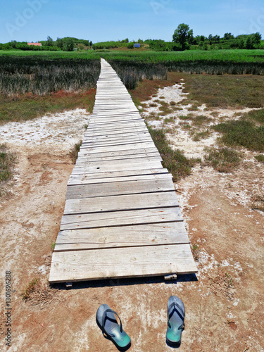 Wooden boardwalk through marshland with abandoned flip-flops in foreground