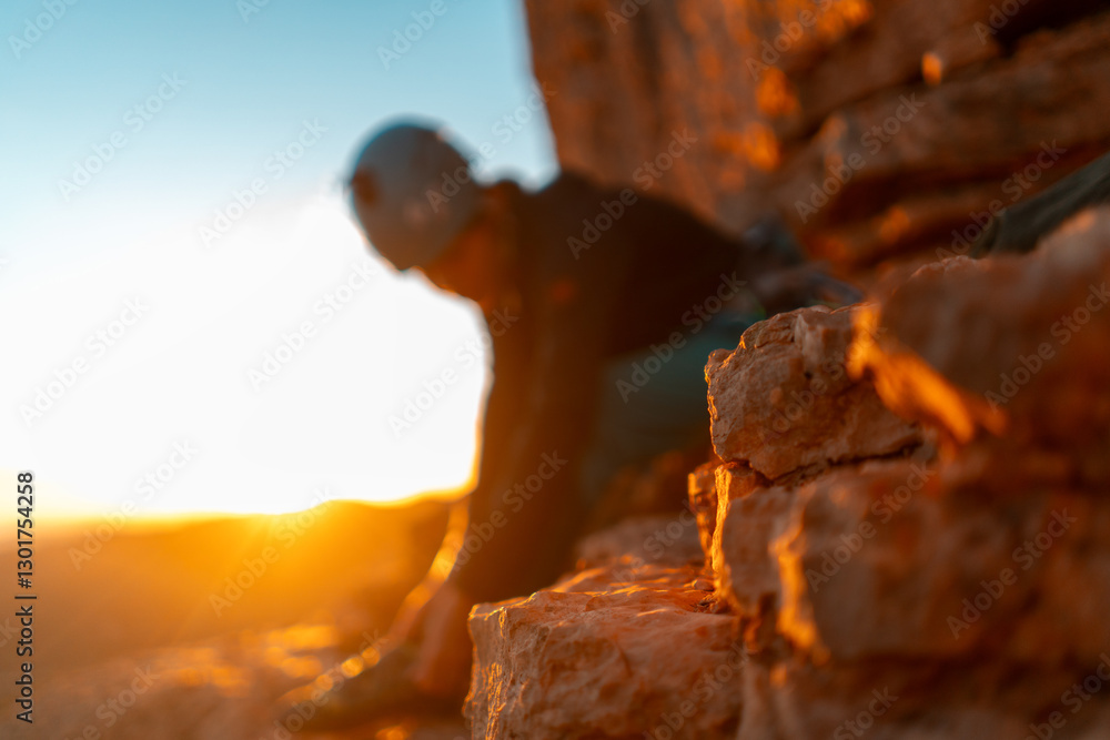 Fototapeta premium Young girl is preparing for training on the rocks sunset, in the mountains and puts a helmet . Woman engaged in active sports, in mountaineering and rock climbing.