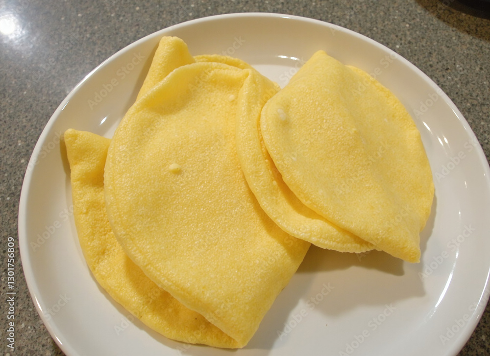 Three golden yellow crepes folded and stacked on a white plate. Three golden yellow crepes folded and stacked on a white plate.