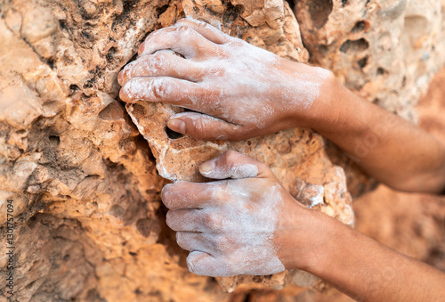 Young girl is engaged in extreme sports, fearlessly climbs up the rock using white magnesia powder, holds her hand to the ledge in the relief,