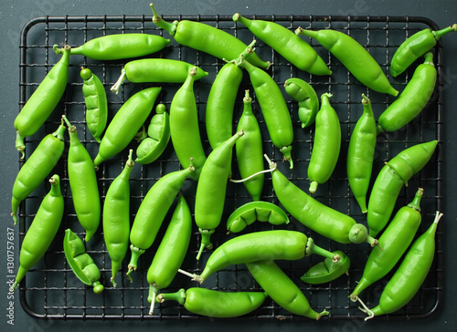 Overhead shot of fresh green peas on a cooling rack against a dark background. photo