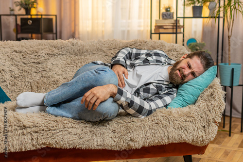 Foto Young ill sick man lying at home with palm on abdomen, quietly moaning from stomach trouble or overeating