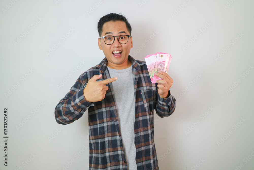 Cheerful handsome young Asian man pointing fingers at money banknotes isolated on white background Cheerful handsome young Asian man pointing fingers at money banknotes isolated on white background