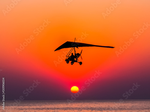 Fotografie Motorized glider flies against the sunset over the sea.