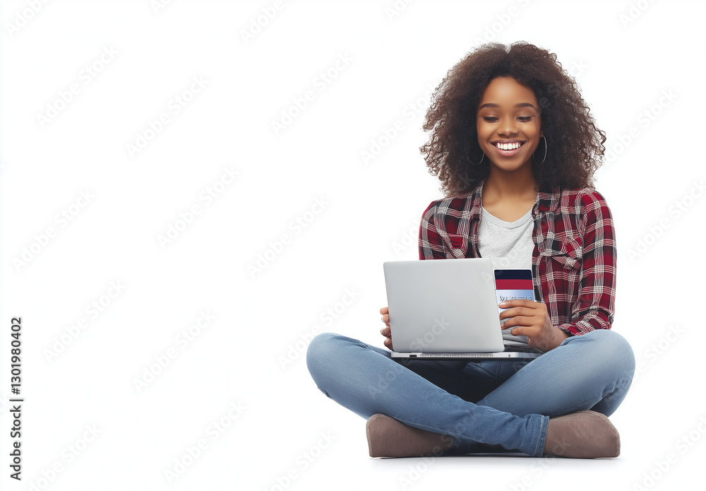 Fototapeta premium A happy woman sitting on the floor with her legs crossed, holding an open credit card in one hand and using a laptop computer to make online purchases against a white background