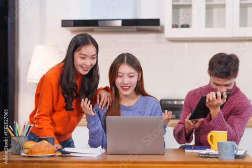 An Asian young woman with college friends sitting at a table, looking at a laptop, studying online at home, having a fun party, sharing stories, talking, and enjoying a friendly get-together