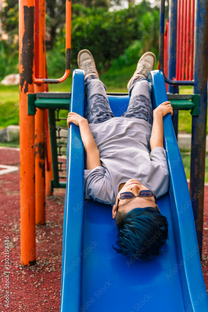 Obraz premium Photo of a Colombian Latino mestizo pre-teen with blue hair lying on a slide with his head down