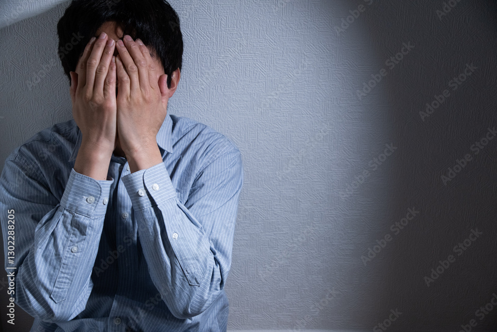 顔を覆い隠し落ち込む男性とスポットライト