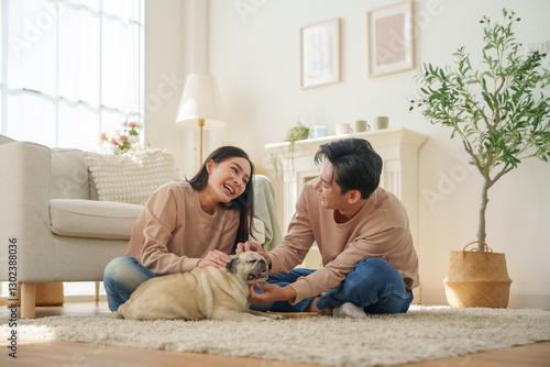 Asian couple shares a joyful moment while playing with their pet dog in a living room. relaxation and bonding.