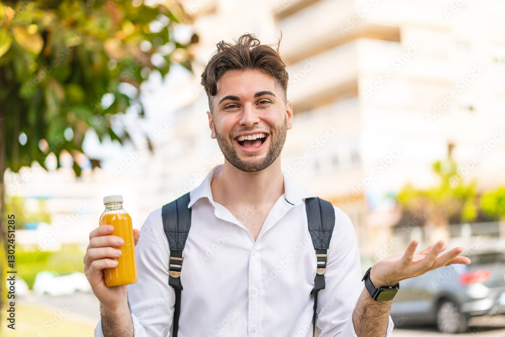 Fototapeta premium Young handsome man holding an orange juice at outdoors with shocked facial expression