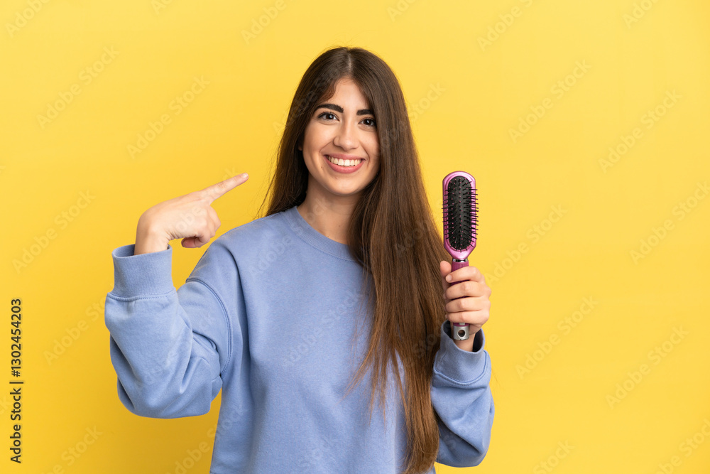 Young caucasian woman holding hairbrush isolated on blue background giving a thumbs up gesture Young caucasian woman holding hairbrush isolated on blue background giving a thumbs up gesture