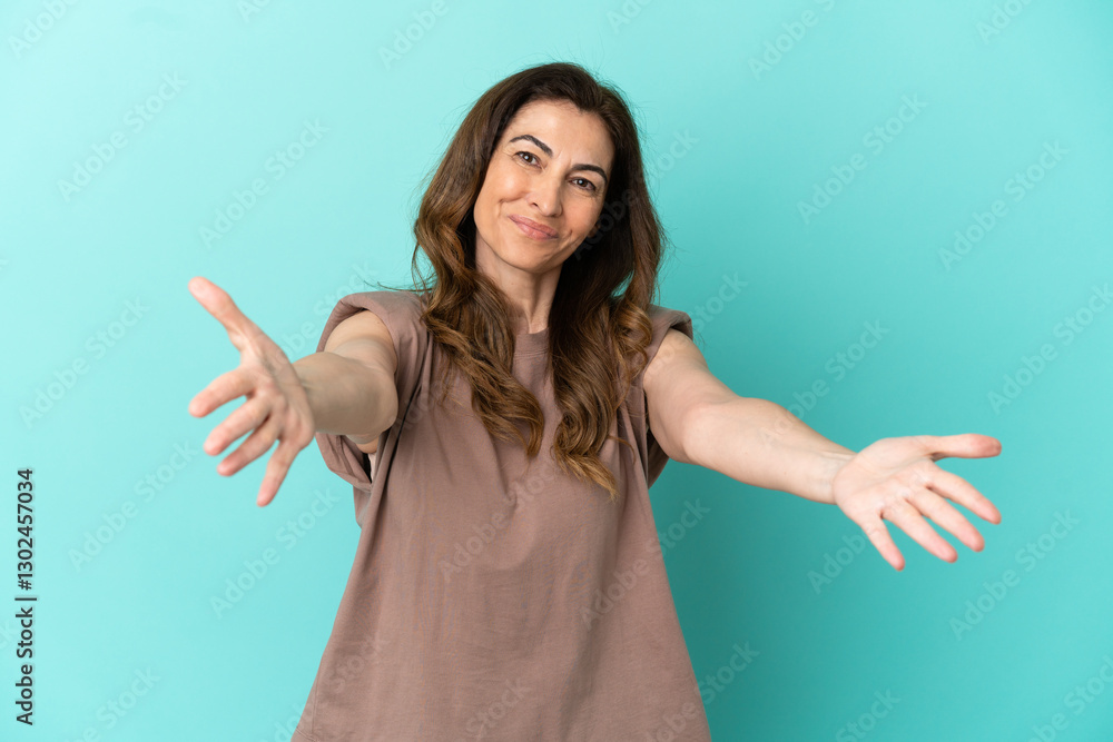 Fototapeta premium Middle aged caucasian woman isolated on blue background presenting and inviting to come with hand