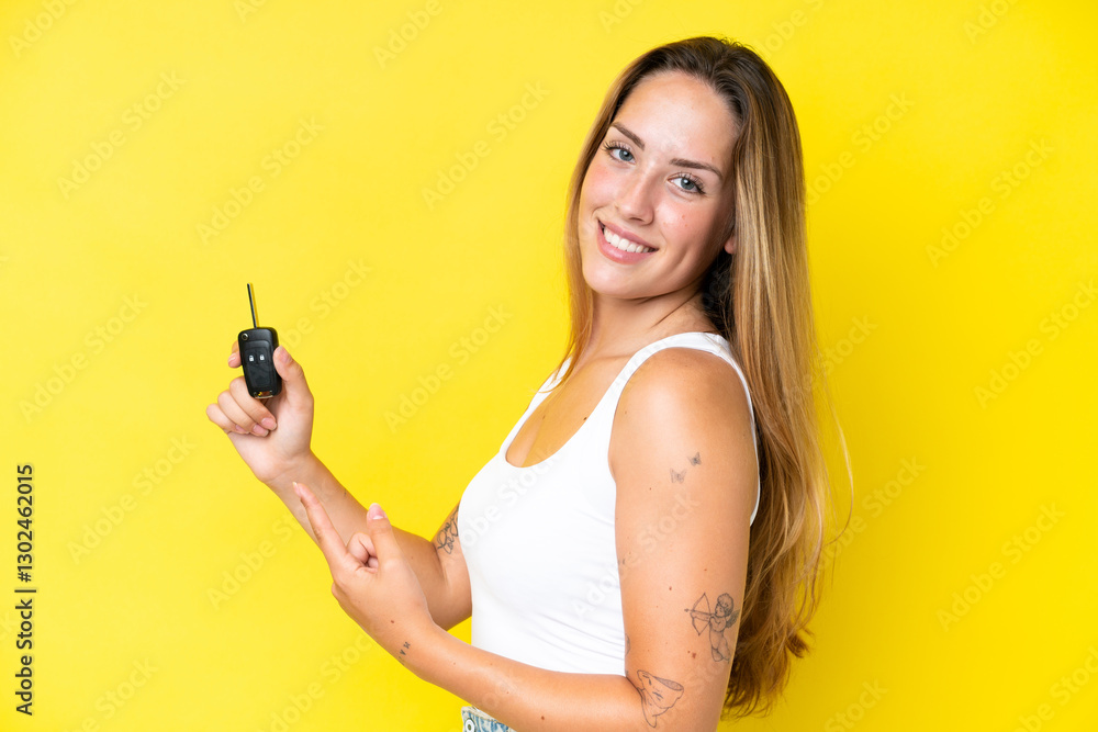 Young caucasian woman holding car keys isolated on yellow background and pointing it Young caucasian woman holding car keys isolated on yellow background and pointing it
