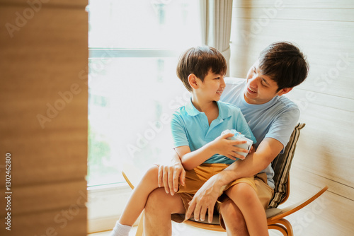 Asian boy give a gift box to his father, Dad and son embrass each other with love and happiness, Relationship in family concept. Celebrate for father day and birthday in living room. photo