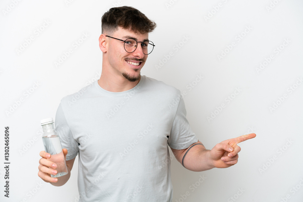 Young caucasian man holding a bottle of water isolated on white background surprised and pointing finger to the side Young caucasian man holding a bottle of water isolated on white background surprised and pointing finger to the side