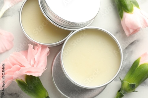 Moisturizing lip balms and pink flowers on white marble table, flat lay photo