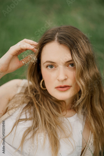 A young woman holding flower in her head, with smooth skin lying on a grass. 