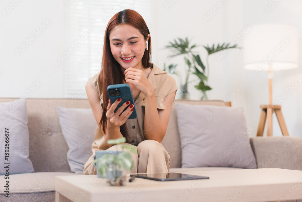 Asian businesswoman sitting on sofa, holding smartphone and coffee mug, smiling in cozy living room. Asian businesswoman sitting on sofa, holding smartphone and coffee mug, smiling in cozy living room.