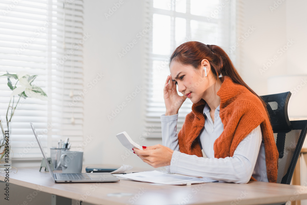Cheerful Asian businesswoman celebrating success while looking at her smartphone, sitting at desk with laptop and glasses.