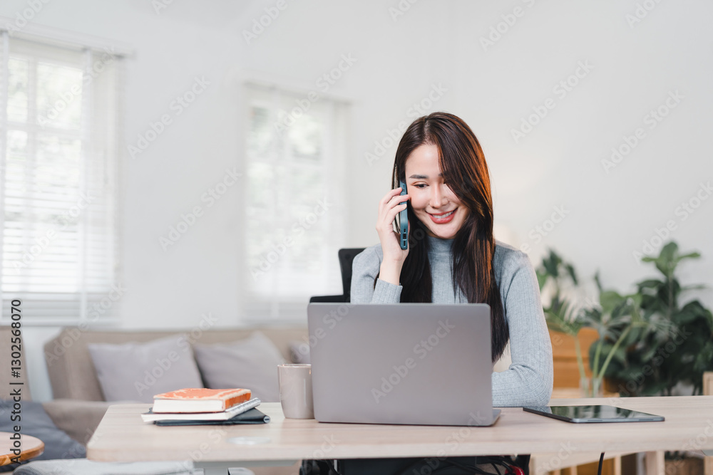 Asian businesswoman in red sweater working at desk with laptop, sticky notes, and stationery in bright office. Asian businesswoman in red sweater working at desk with laptop, sticky notes, and stationery in bright office.