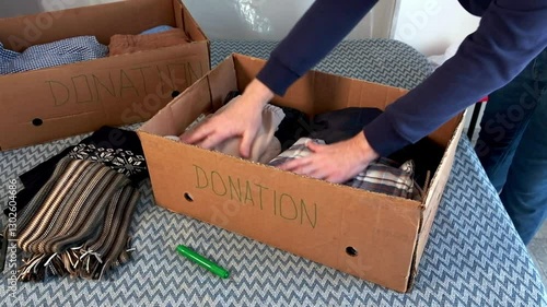 Sorting clothes for donations. Cardboard donation box with things.
