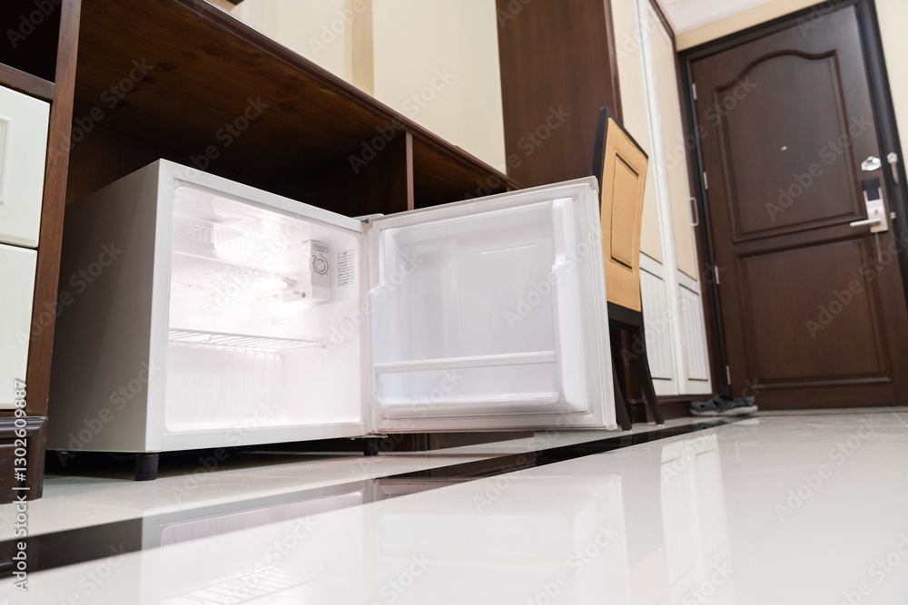 mini fridge in low angle view, inside it’s empty shelves placed under wooden counter and next to wood closet and chair in a luxury hotel room. mini fridge in low angle view, inside it’s empty shelves placed under wooden counter and next to wood closet and chair in a luxury hotel room.
