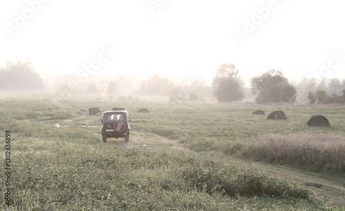 Jeep Driving Through Misty Field with Hay Bales