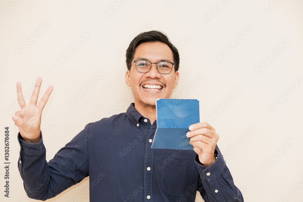 A Southeast Asian man smiling happily while holding his savings book and giving number 12345 by hand gesture in isolated cream background, bank and finance concept A Southeast Asian man smiling happily while holding his savings book and giving number 12345 by hand gesture in isolated cream background, bank and finance concept
