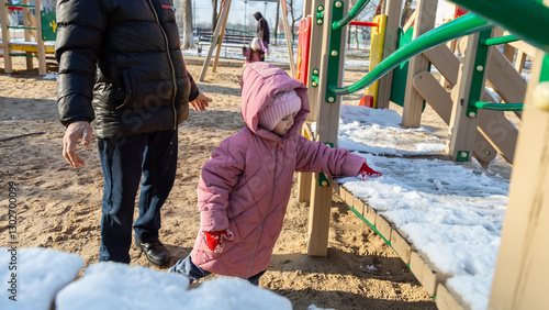 Grandfather playing with his granddaughter on the playground in the park in winter
