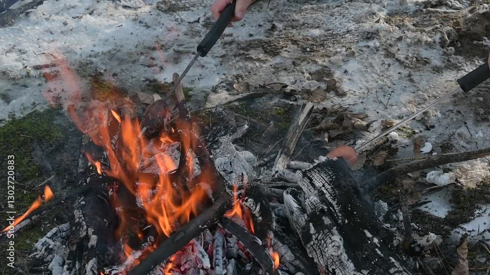 A people gathers around a crackling fire, roasting sausages on sticks during a cold winter day. A people gathers around a crackling fire, roasting sausages on sticks during a cold winter day.
