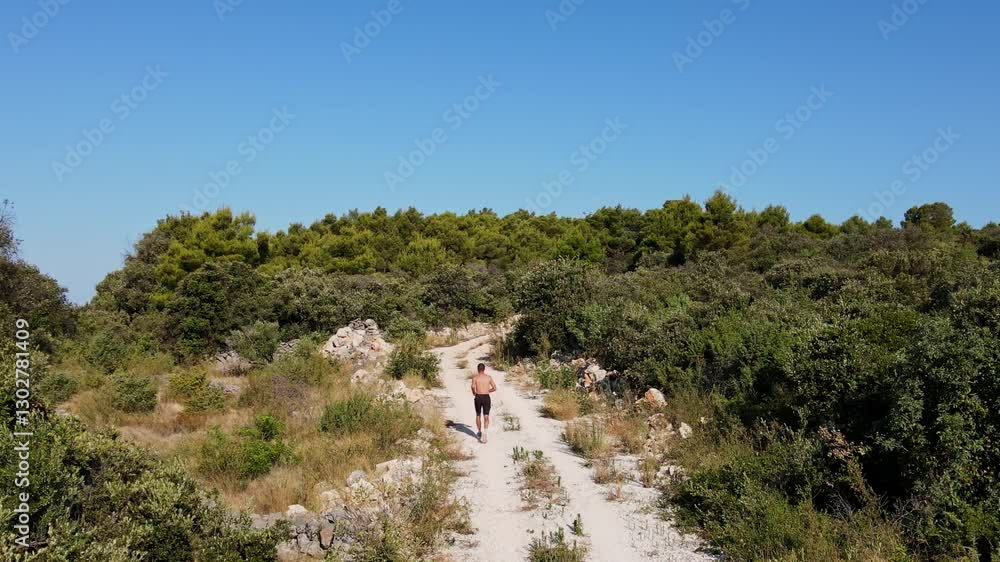 Shirtless man jogging on dirt trail in hot sunny day, surrounded by lush green nature, aerial view. Professional athlete training endurance outdoor. Trail running and fitness concept Shirtless man jogging on dirt trail in hot sunny day, surrounded by lush green nature, aerial view. Professional athlete training endurance outdoor. Trail running and fitness concept