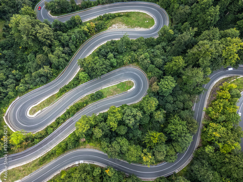 zenithal aerial view of a winding 180-degree curved road in a green forest while cars pass by on the road in Romania.
