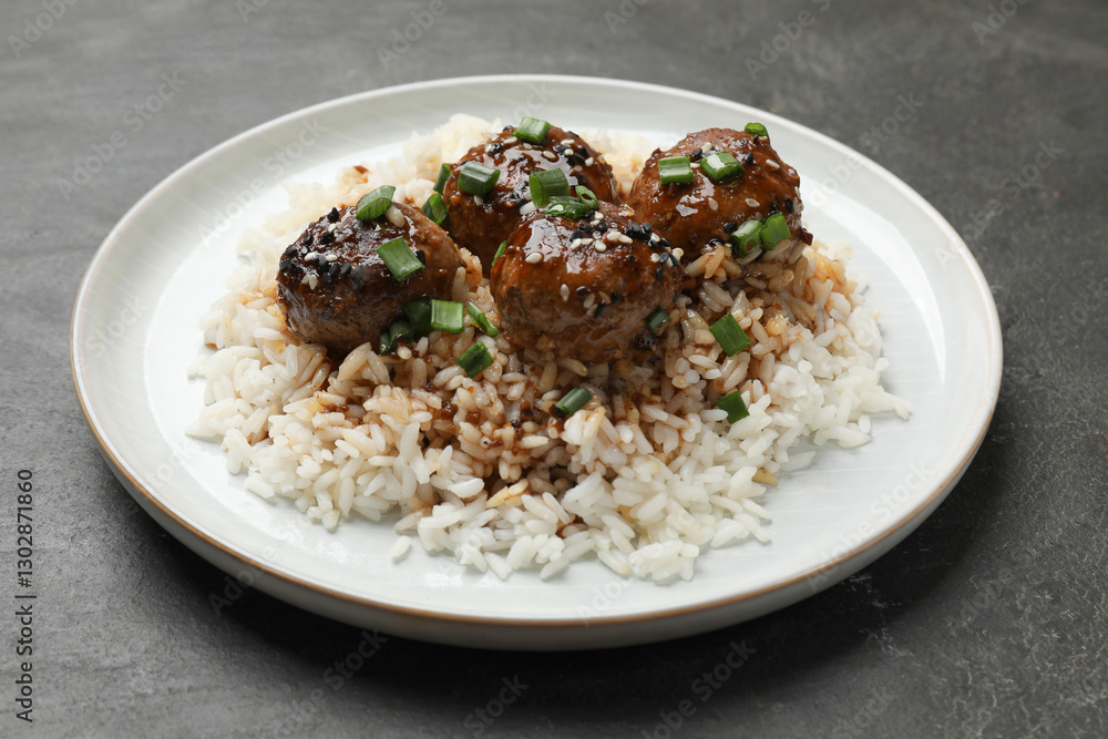 Delicious rice with meatballs, sauce and green onions on black table, closeup Delicious rice with meatballs, sauce and green onions on black table, closeup