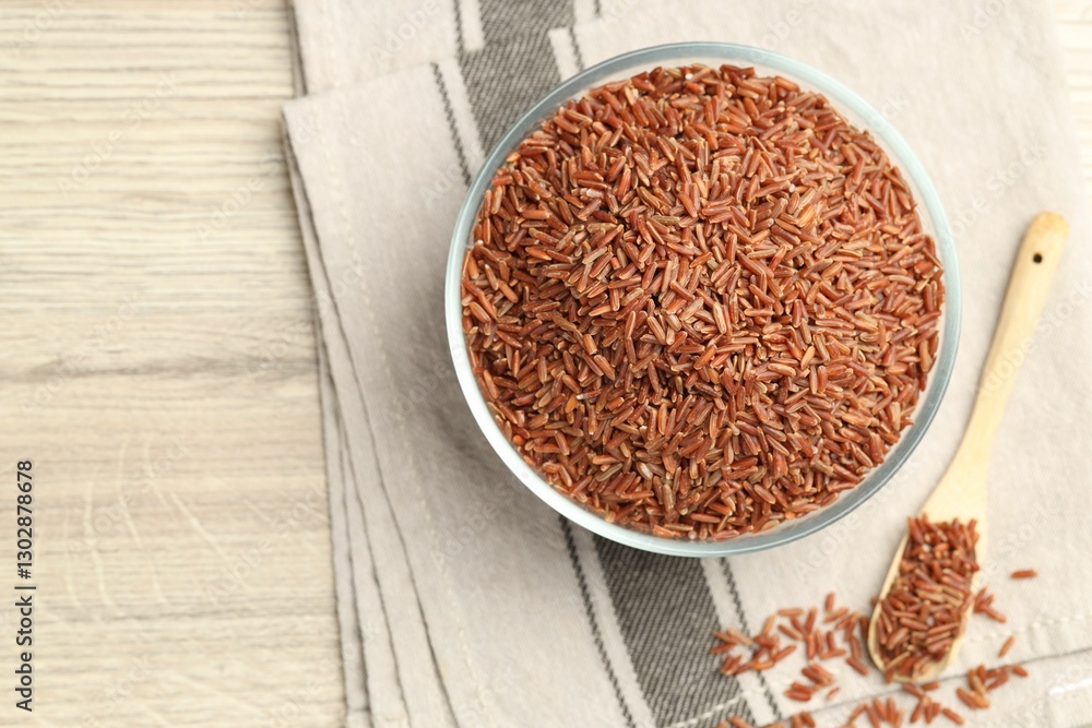Brown rice in glass bowl and spoon on wooden table, flat lay. Space for text Brown rice in glass bowl and spoon on wooden table, flat lay. Space for text