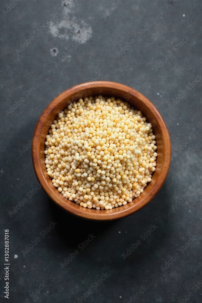 Overhead View of Small Round Yellow Grains in Wooden Bowl on Dark Surface Overhead View of Small Round Yellow Grains in Wooden Bowl on Dark Surface