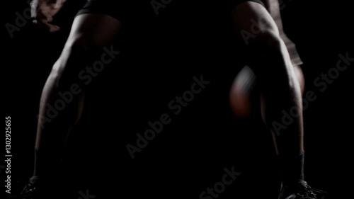 Basketball player bouncing a ball. African american sports man practicing against black background. Abstract body shot front view.