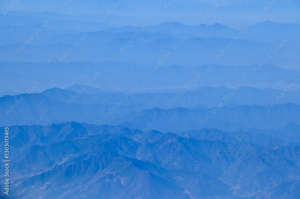 Fototapeta premium The view of the stunning landscape with mountains and clouds from the airplane window. Aerial view of the natural scene, mountain range. Travel and landscape scene. Travel and nature concept. 