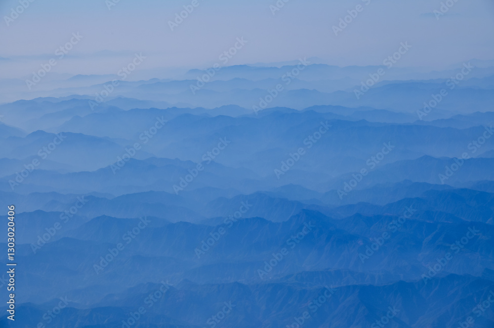 Obraz premium The view of the stunning landscape with mountains and clouds from the airplane window. Aerial view of the natural scene, mountain range. Travel and landscape scene. Travel and nature concept.