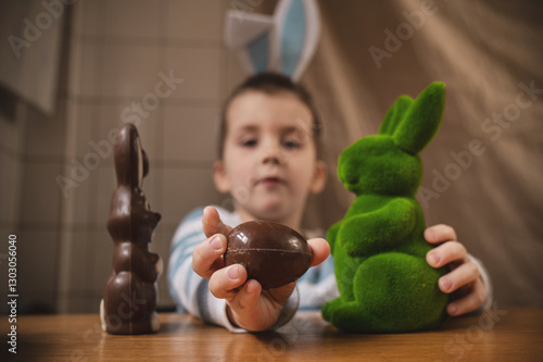 Boy with bunny ears 5 years old playing with Easter bunnies at table closeup,  Easter celebration traditions, celebration, colorful spring in cozy home environment, spring colors
chocolate agg in hand photo