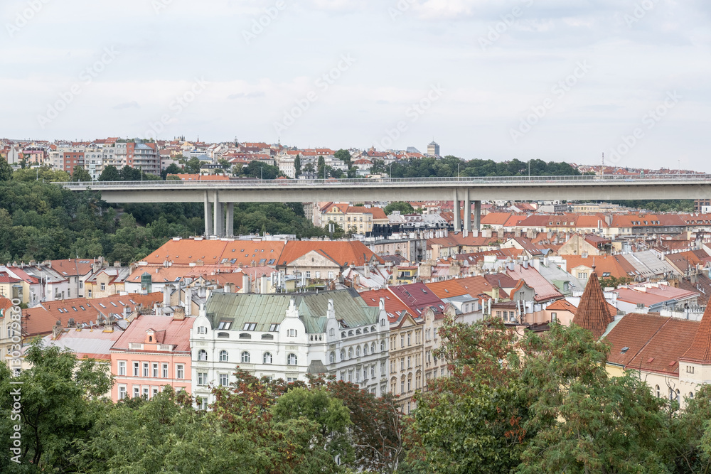 Obraz premium Nusle Bridge, Prague, Czech Republic – 24.07.2024. A cityscape with red-roofed buildings and a modern bridge over. Greenery surrounds the historic and contemporary architecture