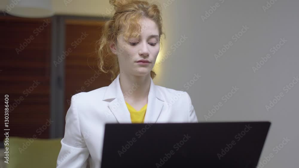Girl wearing formal white jacket working on a laptop computer at home. Serious face expression looking at camera. Horizontal camera movement. Girl wearing formal white jacket working on a laptop computer at home. Serious face expression looking at camera. Horizontal camera movement.